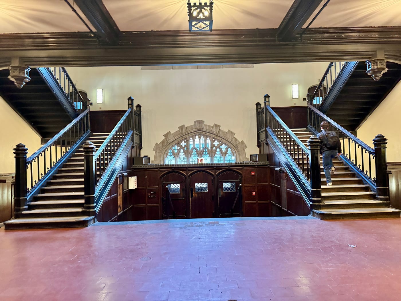 The lobby of Bartlett Dining Commons, with two dark wood staircases and a gothic window, in the university's old gym.