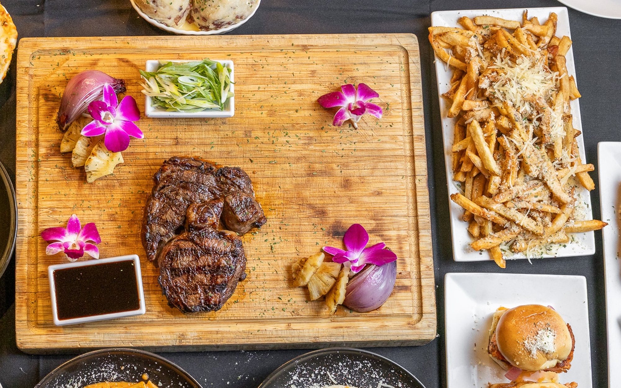 A grilled steak on a wooden board with fries at Chemistry, grilled pineapple and red onion on the side