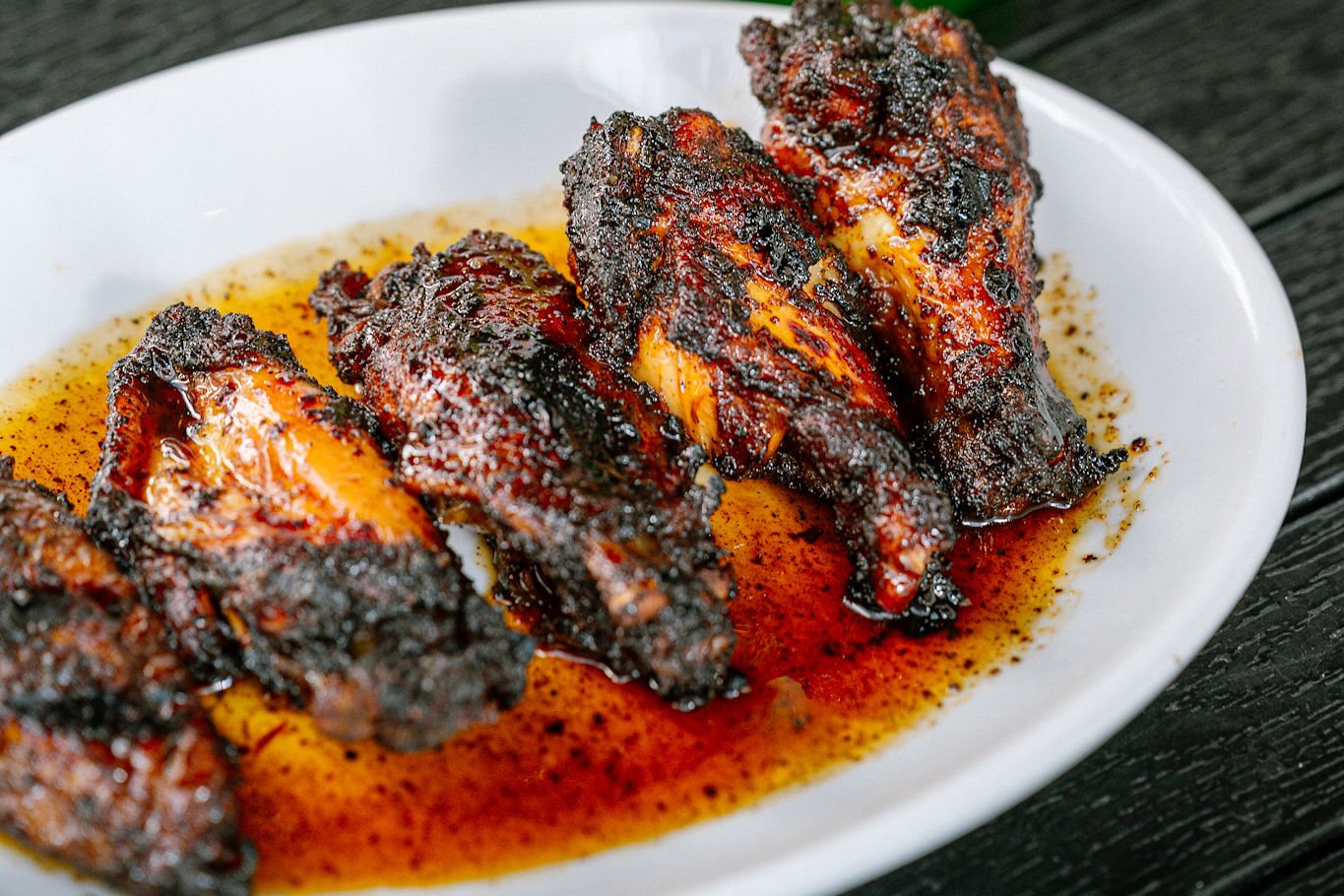 Charred jerk chicken wings glazed in jerk sauce on a white plate at Ja' Grill