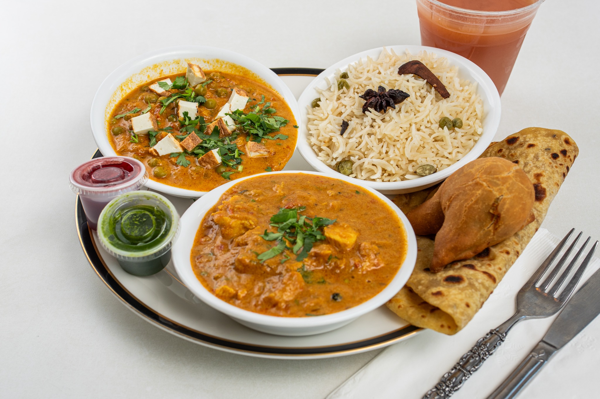A Rajun Cajun combo plate with two curries, pea rice, a paratha, a samosa and tamarind and mint chutneys
