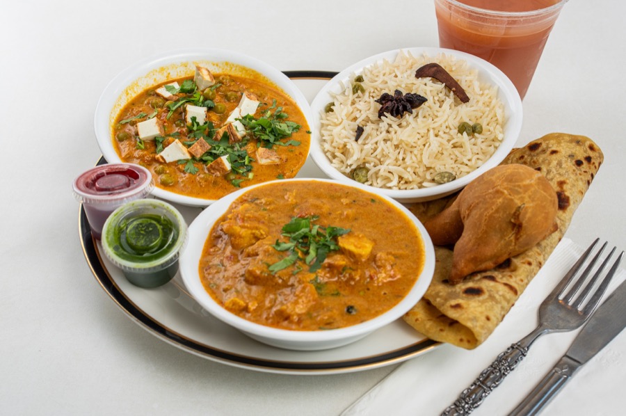 A Rajun Cajun combo plate with two curries, pea rice, a paratha, a samosa and tamarind and mint chutneys